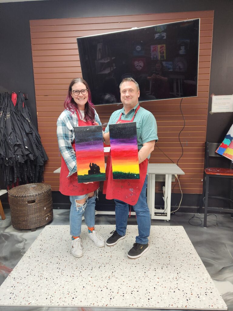 Couple Holding Painted Canvases Together In Cheers N Paint Art Studio In Cary, Nc