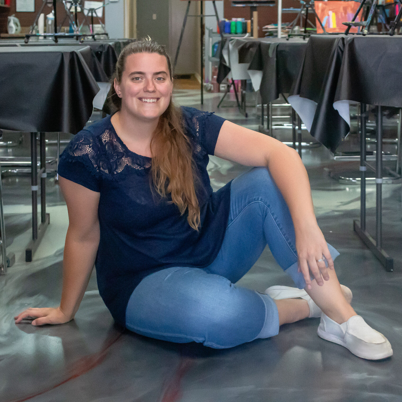 Lauren Salza, Cheers N Paint Studio Owner And Teacher In Cary, Nc Sitting On The Floor After An Art Class Wearing A Blue Shirt.